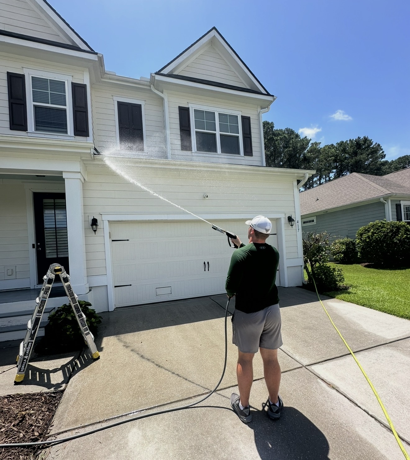 Technician soft washing the siding above a garage on a two-story home