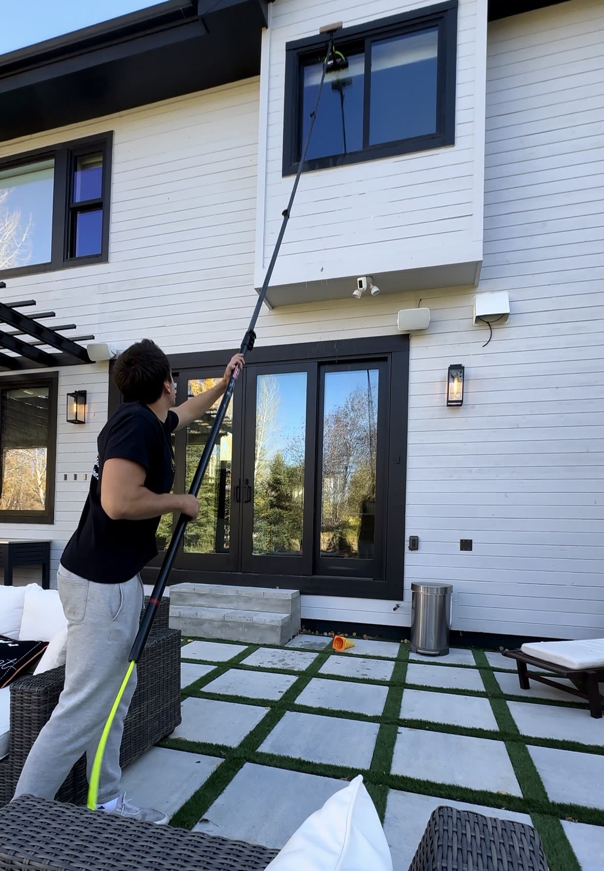 Technician using a water-fed pole to clean upper windows on a white home