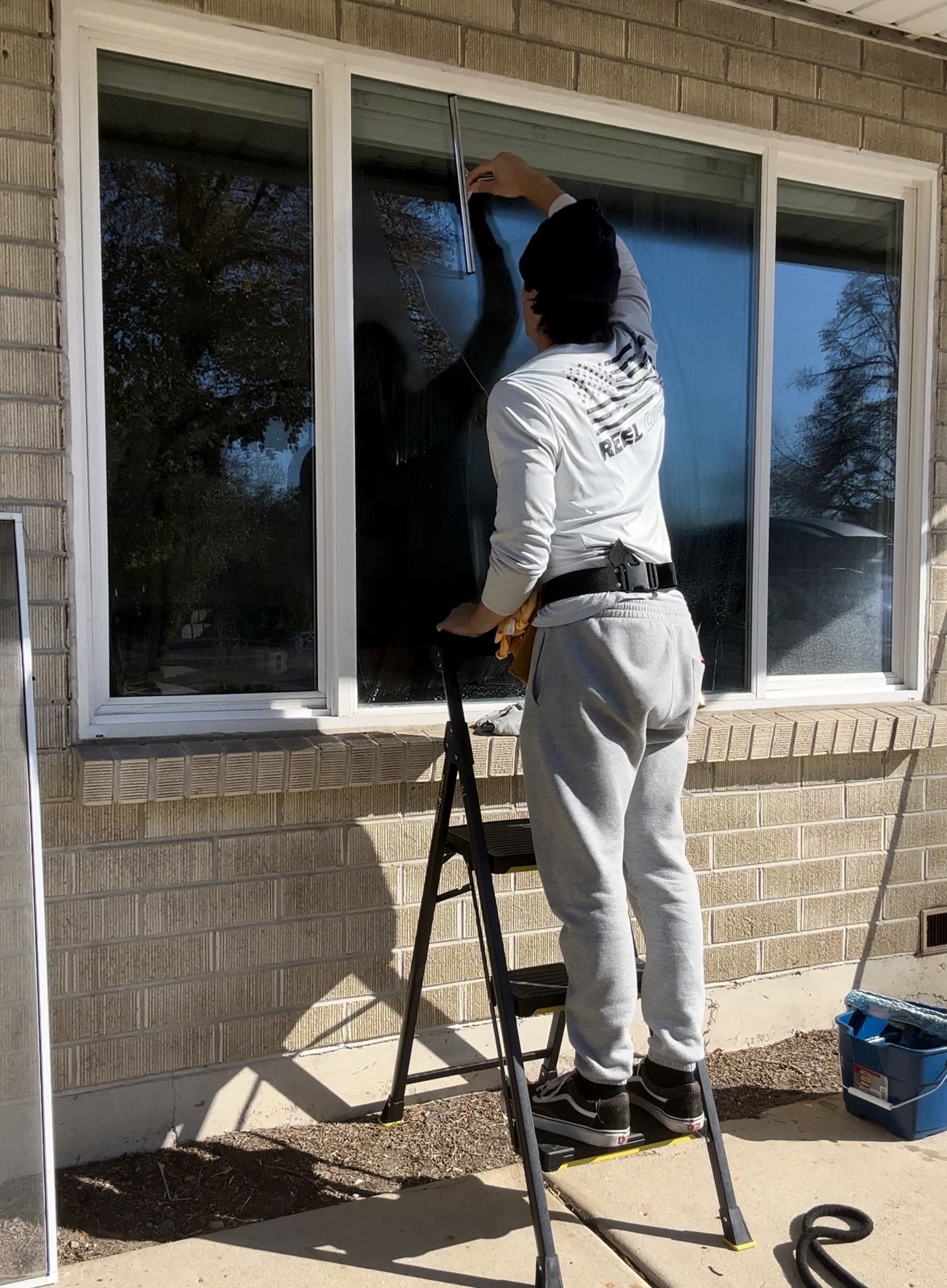 Technician on a step ladder squeegeeing a large picture window on a brick home
