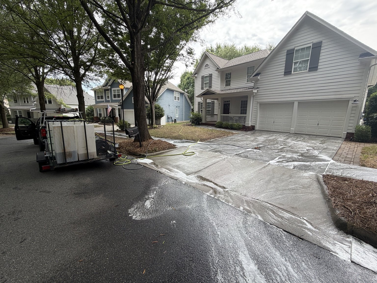 Residential driveway covered in concrete cleaning solution while Tradition Exteriors equipment and work vehicle stand nearby