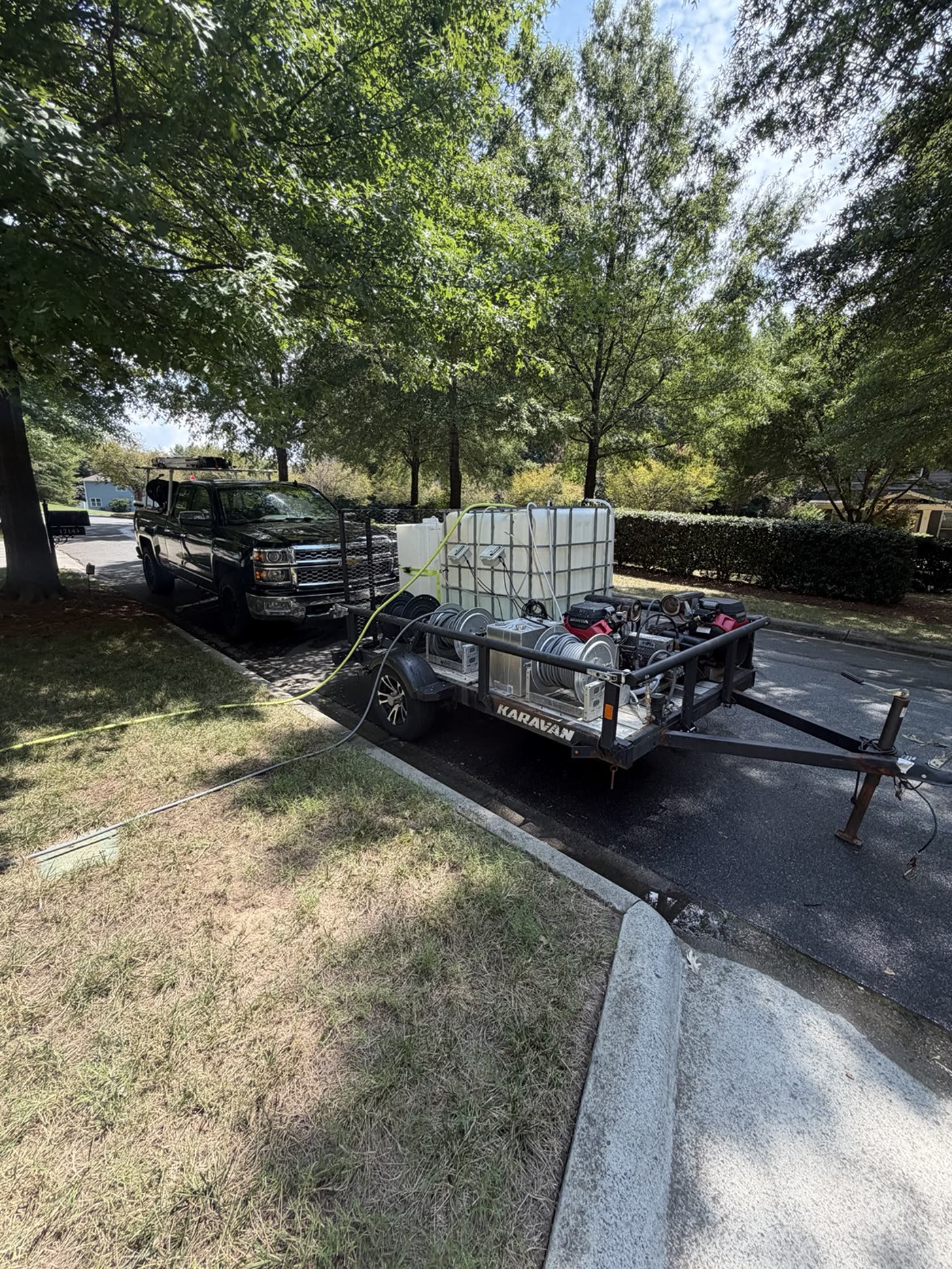 Tradition Exteriors truck and equipment trailer with a dual-machine pressure washing setup, water tanks, and hose reels parked at a job site