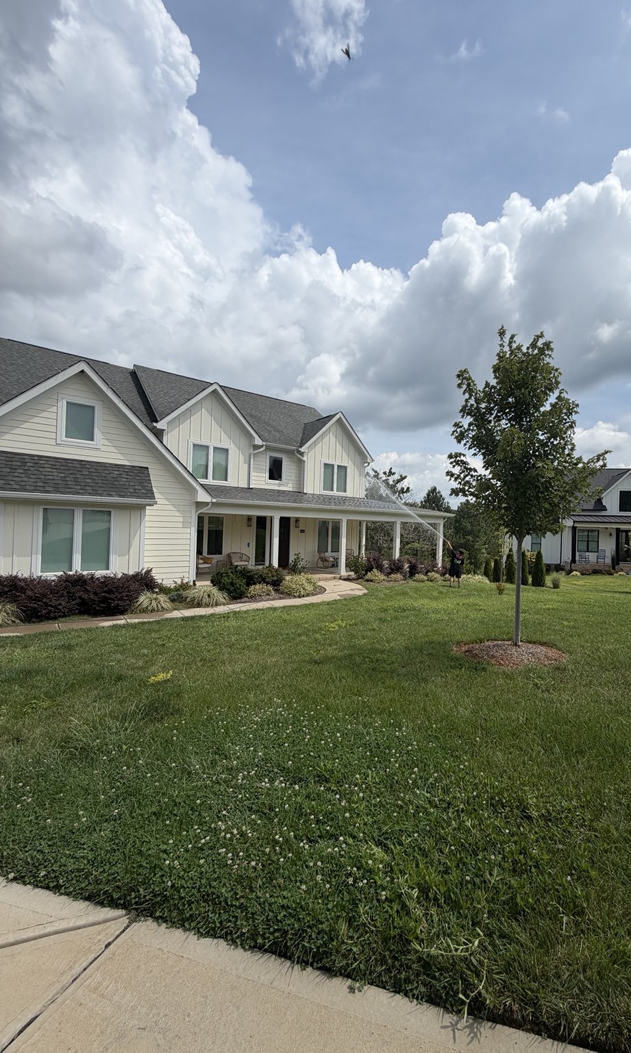 Tradition Exteriors technician soft washing the front of a large two-story home from the lawn